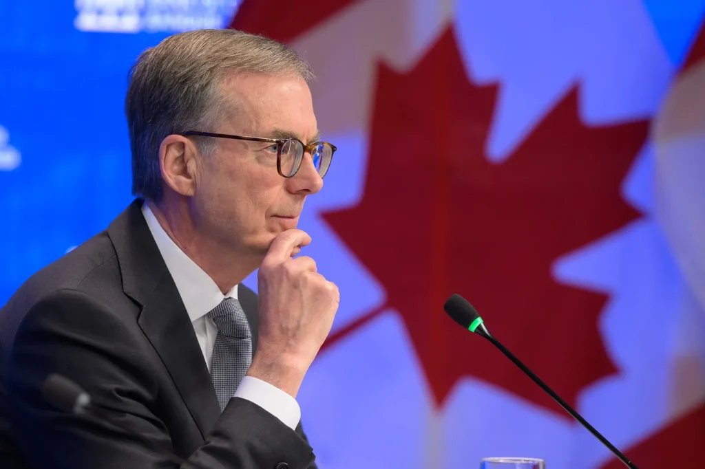 Bank of Canada governor speaking at a press conference in front of a Canada flag
