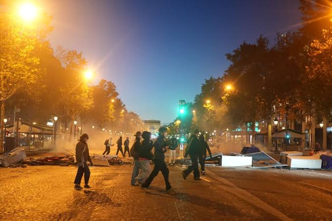 People walking through a street in Paris at night amid debris from unrest
